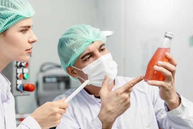 Two scientists pointing at a bottle or red liquid